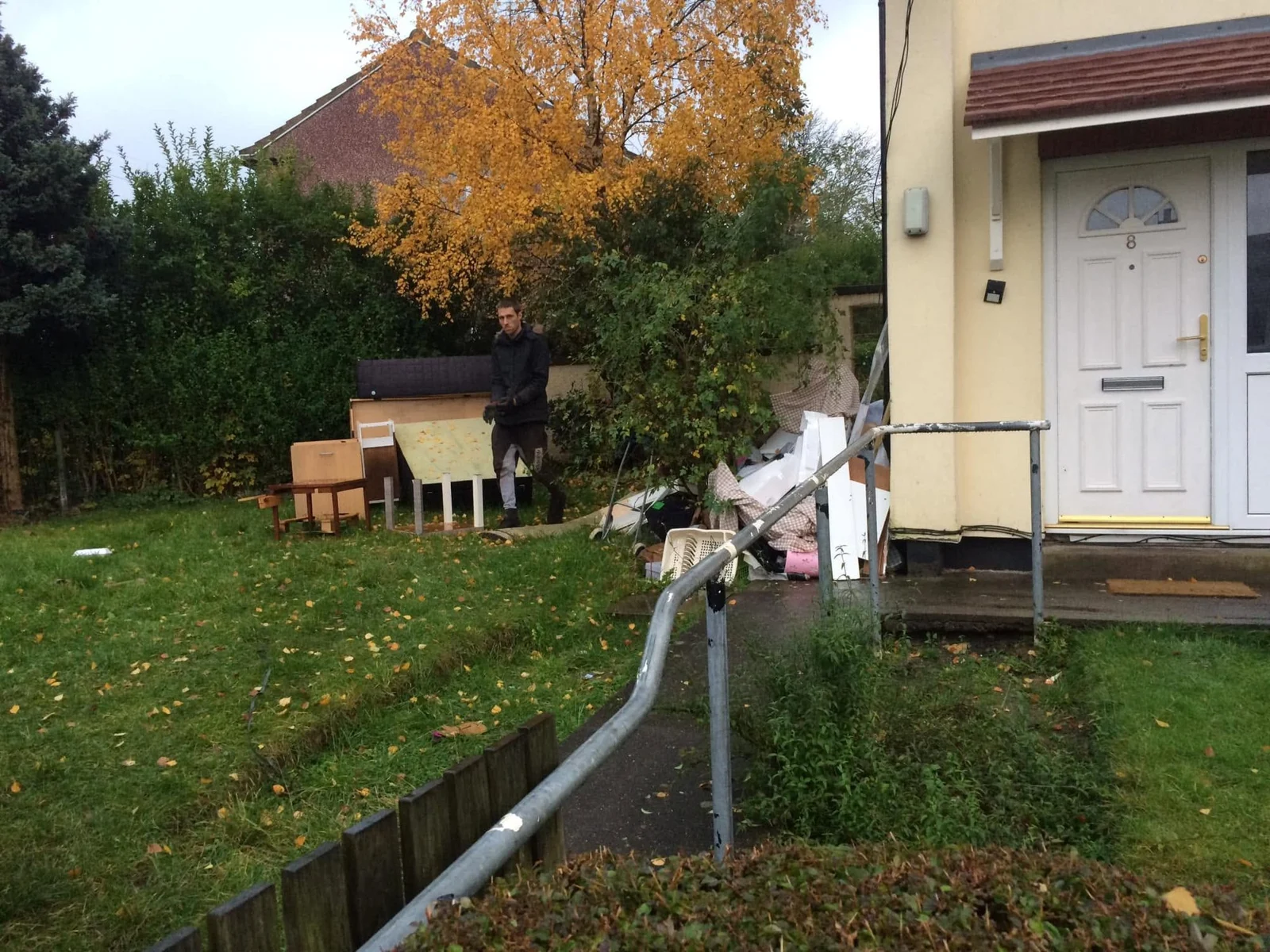 Dismantled wooden furniture and chairs outside a home with a person handling a furniture panel