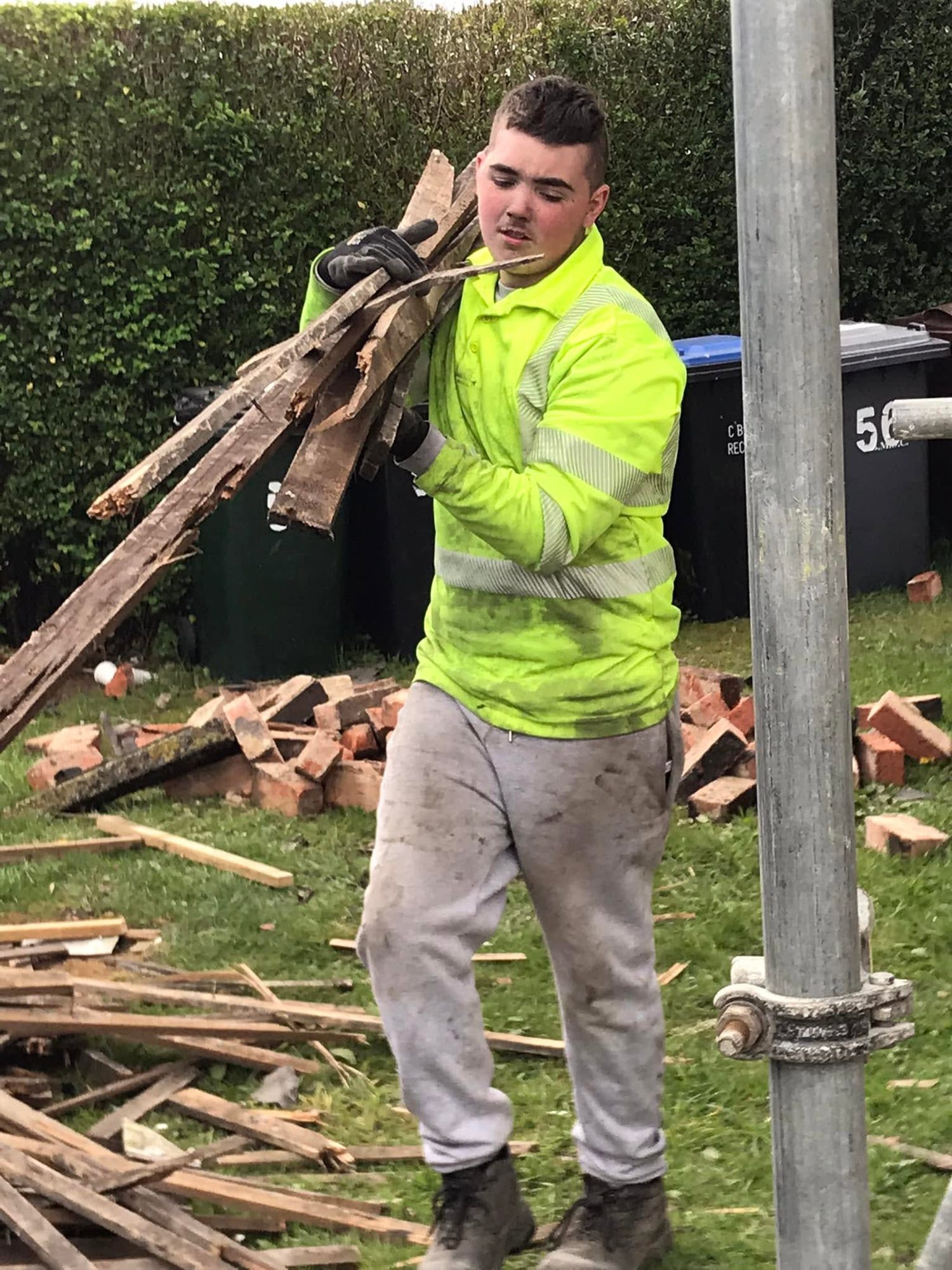 Worker holding timber beside construction debris