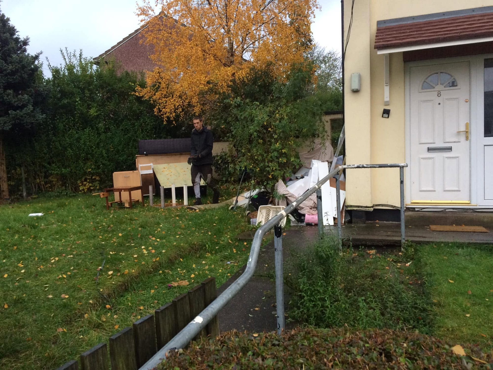Dismantled wooden furniture and chairs outside a home with a person handling a furniture panel