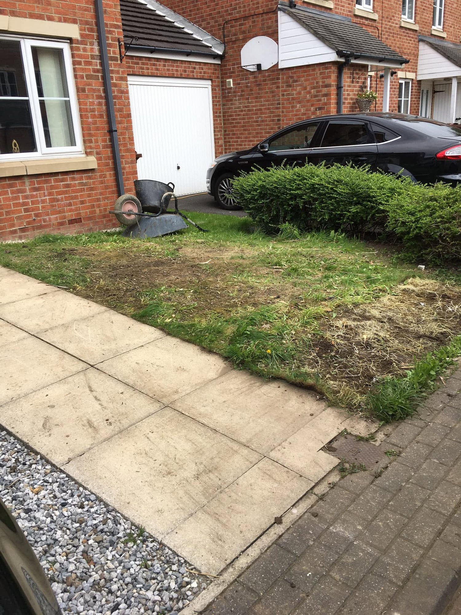 Garden path, lawn and wheelbarrow beside a parked car