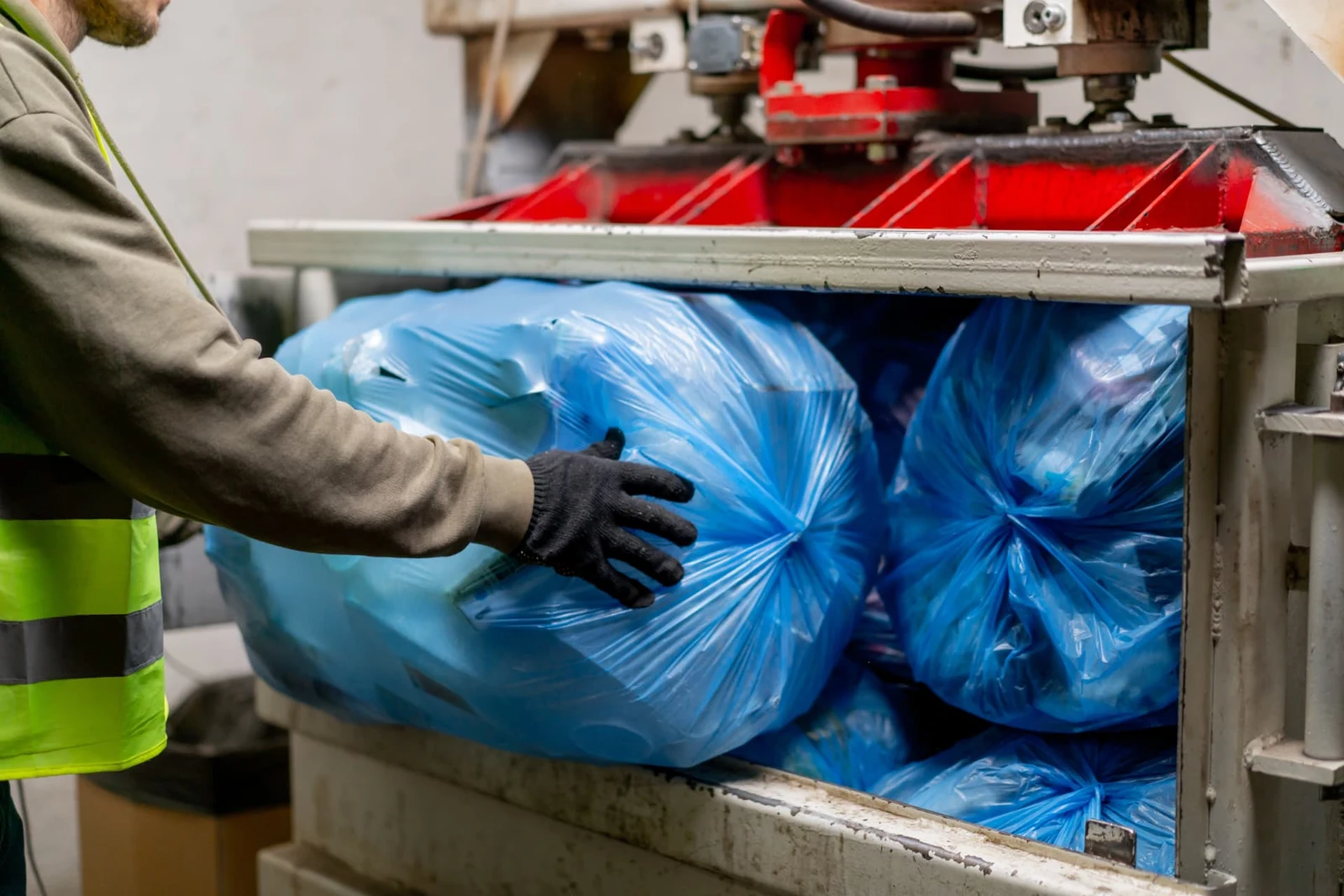 Worker loading blue waste bags into waste-processing equipment